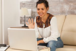 Freelancer waving in video call while working on laptop from home.